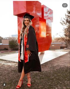 a woman standing in front of a large red sculpture wearing a graduation cap and gown