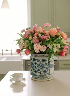 a blue and white vase filled with pink flowers on top of a counter next to a cup