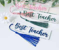 three wooden name tags with tassels and flowers in the background on a white surface