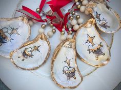 five decorated oysters on a white plate with red ribbon and decorations around them for christmas