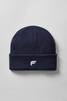 a navy beanie hat with white logo on the front and side, against a gray background