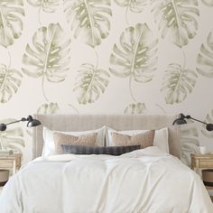 a bed with white sheets and pillows in front of a green leaf wallpaper design