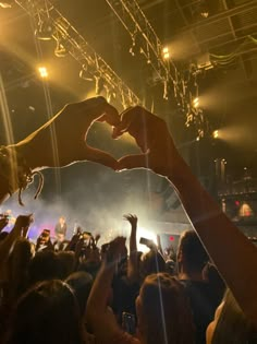 two hands in the shape of a heart are held up by people at a concert