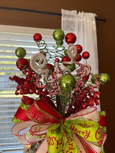 a christmas tree decorated with ornaments and ribbons in front of a window, next to a white curtain