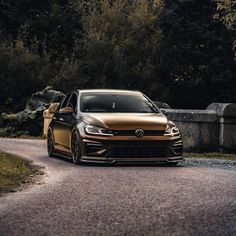 a gold volkswagen golf gtr parked on the side of a road with trees in the background