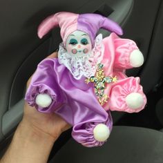 a hand is holding a small doll in the passenger seat of a car, wearing a purple and pink dress