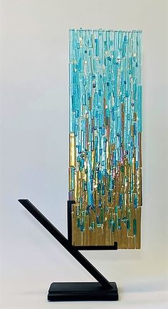 a blue and gold art piece sitting on top of a black metal stand in front of a white wall