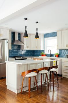 a kitchen with two stools at the island and three lights hanging over the sink