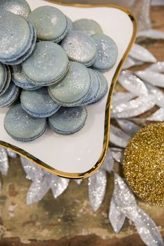 a white plate topped with blue and silver cookies next to a gold glitter ornament