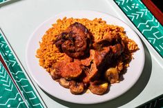 a white plate topped with rice and meat next to a fork on a green table cloth