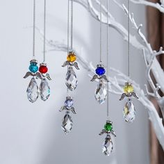 four necklaces hanging from a tree branch with white branches in the foreground and one is multicolored