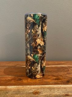 a camo print tumbler cup sitting on top of a wooden table next to a gray wall