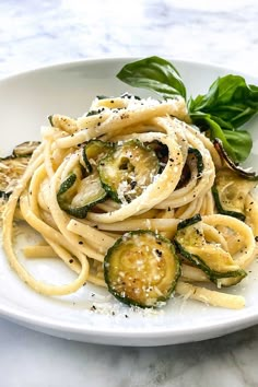 pasta with zucchini, cheese and basil on a white plate sitting on a marble table