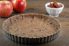 an apple pie sitting on top of a wooden table next to two bowls filled with nuts