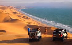 three people standing on top of sand dunes next to vehicles in the middle of the desert