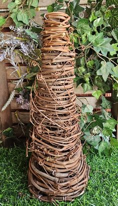 a tall tower made out of wicker sitting in the grass next to a bush