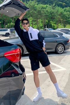 a man is standing in the middle of a parking lot holding up a car hood