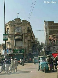 several people are walking down the street in front of some old buildings and cars,