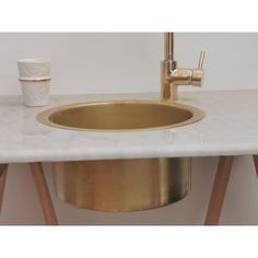 a white counter top with a gold sink and faucet next to a cup