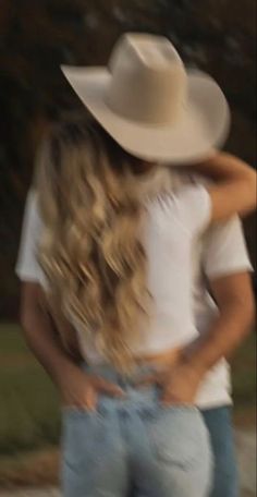 two women in jeans and cowboy hats hugging each other while walking down the street at night