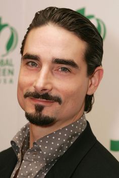 a close up of a person wearing a suit and tie with a moustache