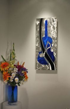 a blue vase with flowers in it sitting next to a wall mounted glass art piece