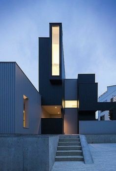 a modern house with stairs leading up to the front door and side windows at dusk