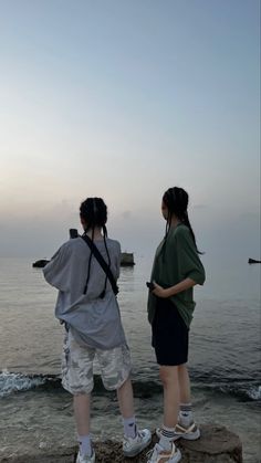 two people standing on the edge of a cliff looking out at the water and land