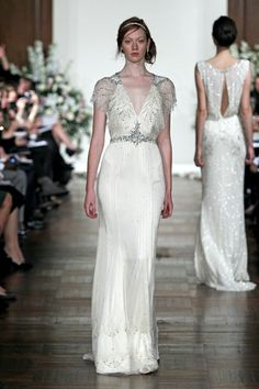 a model walks down the runway in a white gown with beading on her shoulders