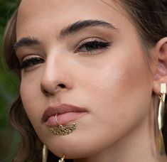 a close up of a woman wearing gold earring and nose ring with leaves on it