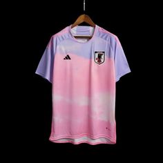 a pink and purple soccer jersey hanging on a hanger in front of a black background