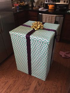 a wrapped present sitting on top of a wooden floor next to a refrigerator freezer