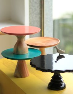 three different colored cake plates sitting on top of a yellow table next to a window