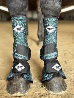 the legs and feet of a horse wearing boots with blue designs on them, standing in dirt