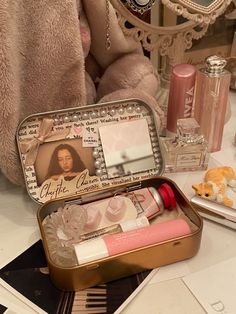 an open tin with various items in it sitting on a table next to a teddy bear