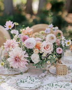 an arrangement of flowers in a vase on top of a table with plates and glasses