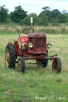 an old red tractor sitting in the middle of a field