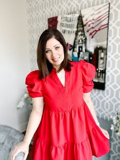 Brunette woman standing in a beautifully fun decorated home wearing a red mini dress with puff sleeves, v neck, tiered skirt. It hits just above the knee. It is perfect for spring and also powerful for work wear as well as great for a date night. Shade Of Red, Little Red Dress, Red Mini Dress, Tiered Skirt