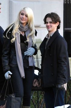 a man and woman standing next to each other on the street with shopping bags in their hands