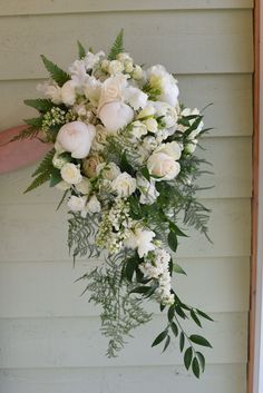 a bouquet of white flowers hanging from the side of a house with greenery on it