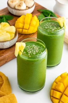 two glasses filled with green smoothie next to sliced pineapples and banana slices