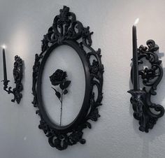 two black candles are lit in front of a mirror and wall with an ornate frame