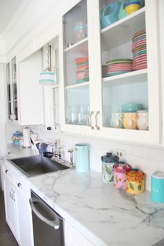 a kitchen with white cabinets and marble counter tops, black dishwasher on the left