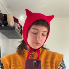 a woman wearing a red knitted cat hat while holding a cell phone in her hands