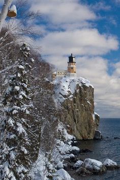 a light house sitting on top of a snow covered cliff next to the ocean and trees