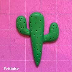 a green cactus brooch sitting on top of a pink tile floor next to a wall