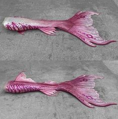 two pink fish sculptures sitting on top of cement floor next to each other, one with its tail curled up