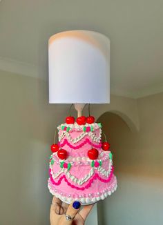 a pink cake with cherries on it being held up by a woman's hand