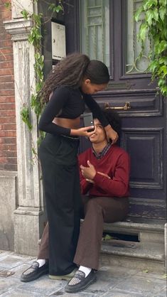 a woman is getting her hair styled by another woman in front of a door with ivy growing on it