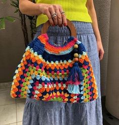 a woman is holding a crocheted bag with tassels on the handles